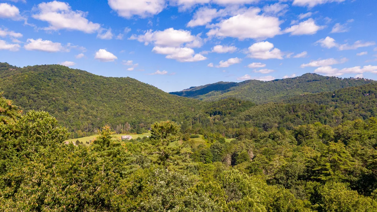 A panoramic view of rolling hills covered in dense trees beneath a blue sky dotted with clouds. The landscape is inviting for hiking, nature walks, and wildlife watching, capturing the spirit of outdoor exploration in the Valle Crucis area.