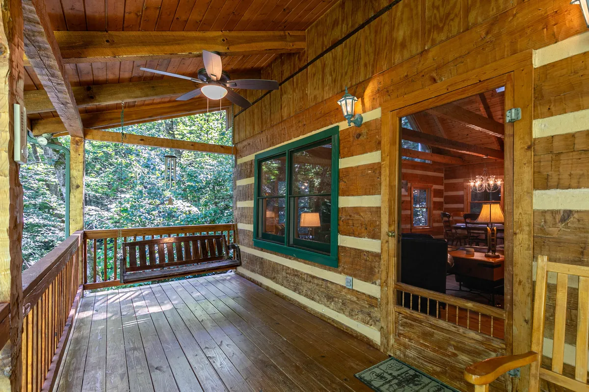 A cozy outdoor porch with a wooden swing, green-trimmed windows, and rustic lanterns. The swing overlooks the tranquil mountain surroundings, offering a peaceful spot for morning coffee, sunset viewing, or quiet moments with family after a day out.
