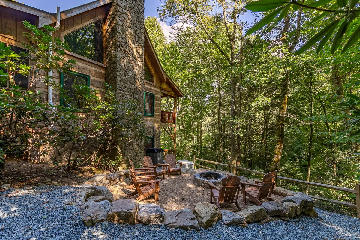 A cozy fire pit area nestled among lush trees, with Adirondack chairs arranged around a stone fire pit. The setting feels intimate and inviting, perfect for gathering under the stars, sharing stories, or making s’mores with family and friends.