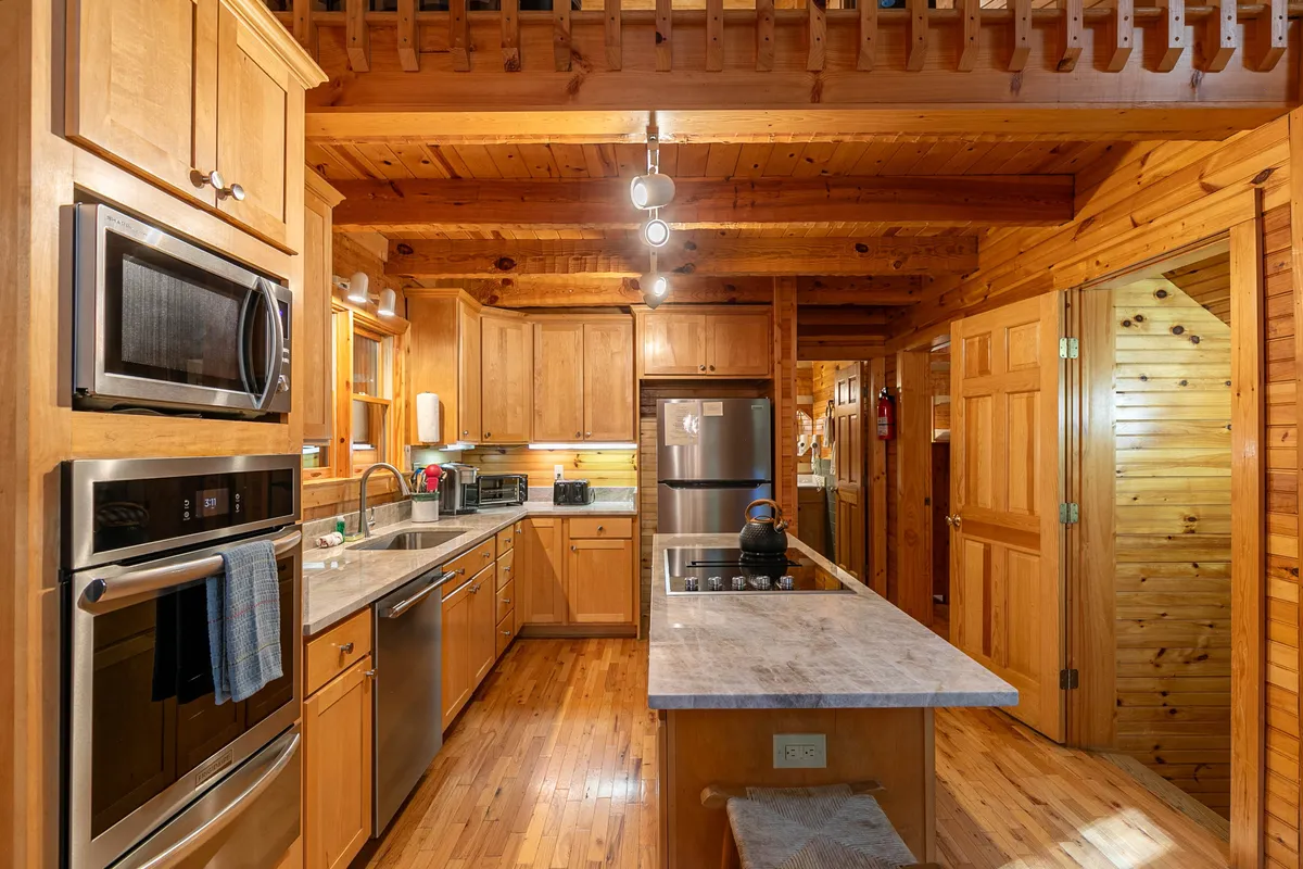 A modern kitchen with wooden cabinetry, a marble (or granite) countertop, a central island, and stainless steel appliances. The space is designed for cooking, baking, and entertaining, inviting both everyday gatherings and special occasions.