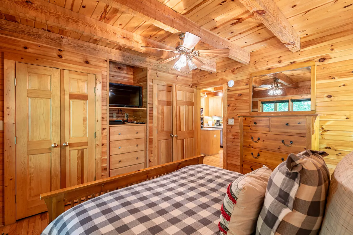 A welcoming bedroom with wooden ceiling beams, plaid bedding, a dresser with a mirror, and wooden doors. The space feels homey and ideal for relaxing after an active day.