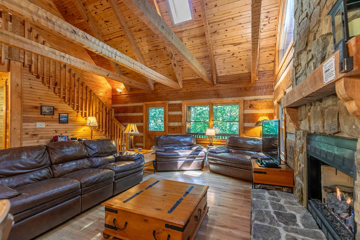A rustic yet elegant living room featuring a stone fireplace, exposed wooden beams, and comfortable leather sofas. The inviting layout suggests a space for winding down together, whether you're reading by the fire or enjoying a quiet evening after an outdoor adventure.